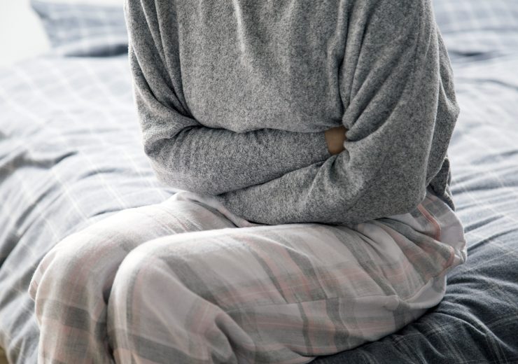Sick woman on bed keeping hands on stomach, suffering from pain