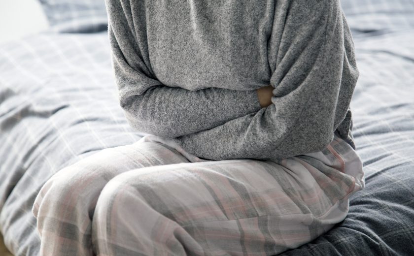 Sick woman on bed keeping hands on stomach, suffering from pain